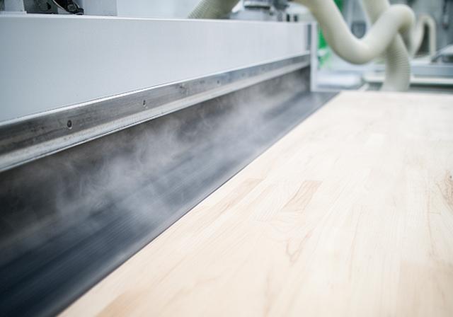 Breitbandschleifmaschine bearbeitet eine helle Leimholzplatte mit feinem Staubabsaugungssystem
